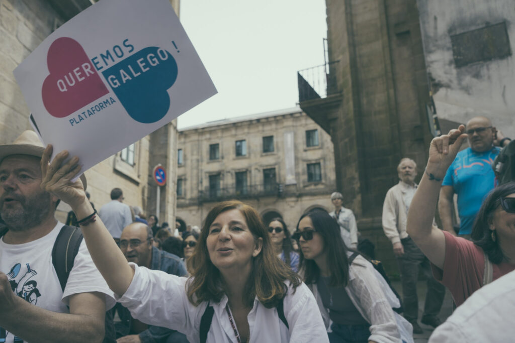 Muller sosteén un cartaz co logotipo de Queremos Gaelgo